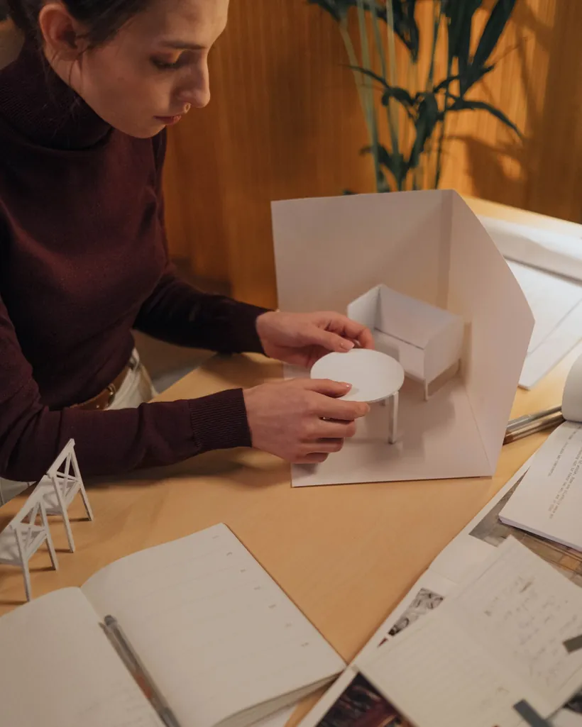 Mesa de taller con recortes de cartón, plantillas y una pequeña maqueta en construcción